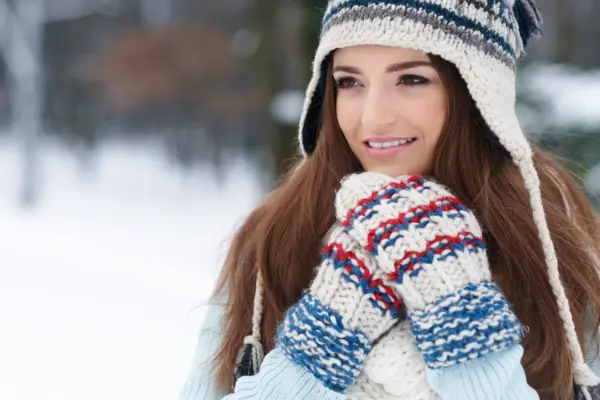 Frau mit Wollmütze und Fäustlingen im Schnee – Schutz vor Kälte bei Hautprobleme im Winter