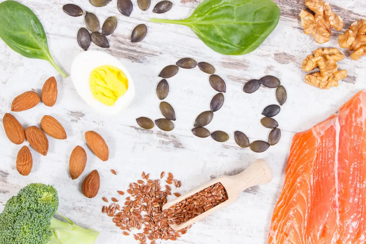 Verschiedene Omega-3-reiche Lebensmittel wie Lachs, Nüsse, Samen, Ei und grünes Gemüse auf hellem Untergrund