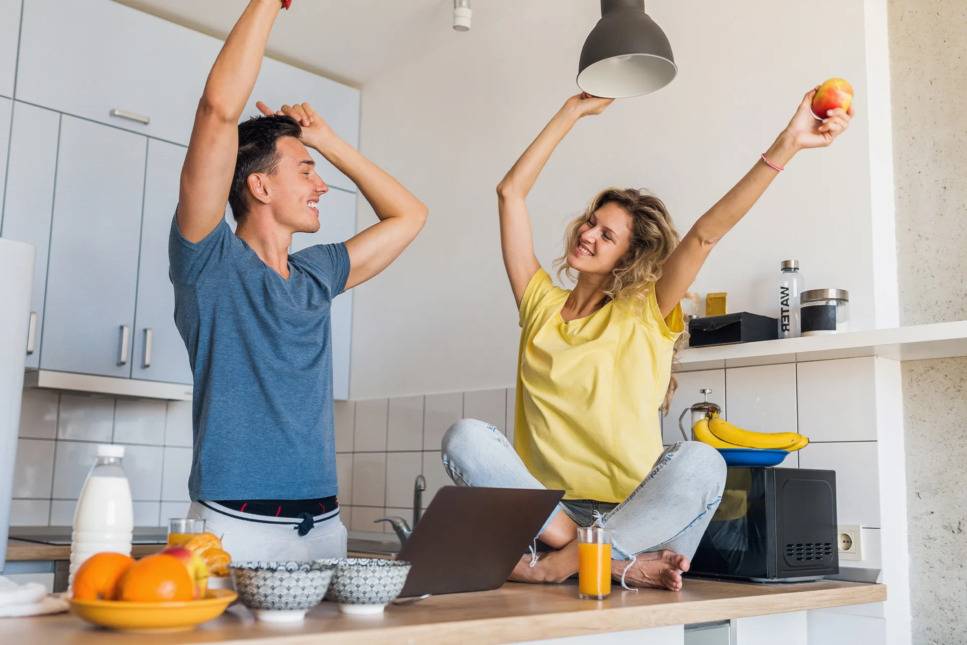 Junges Paar in der Küche, das sich bewegt, lacht und gemeinsam gesund frühstückt als Symbol für Stressabbau und ein starkes Immunsystem