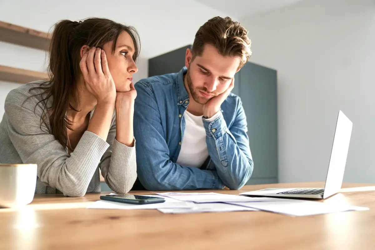 Gestresstes Paar sitzt erschöpft am Tisch vor einem Laptop und Unterlagen als Sinnbild für mentalen Stress und Belastung des Immunsystems