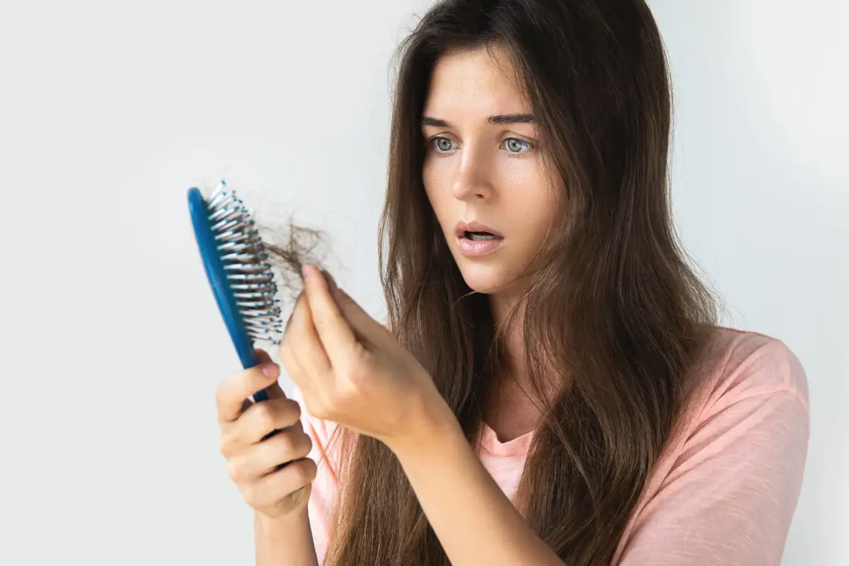 Frau betrachtet besorgt ausgefallene Haare in Haarbürste – mögliche Haarausfall Ursachen