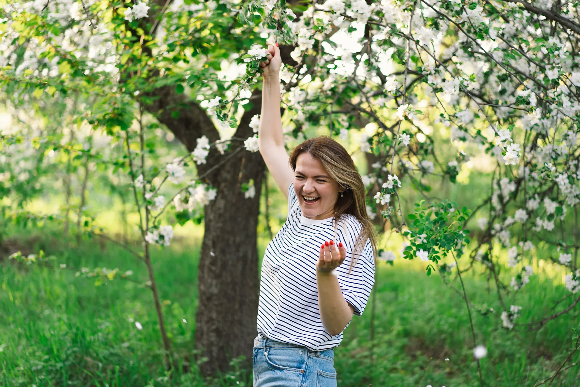 Frau im Frühling in blühender Natur mit erhobenen Armen als Symbol für Energie und Ausgleich bei Frühjahrsmüdigkeit