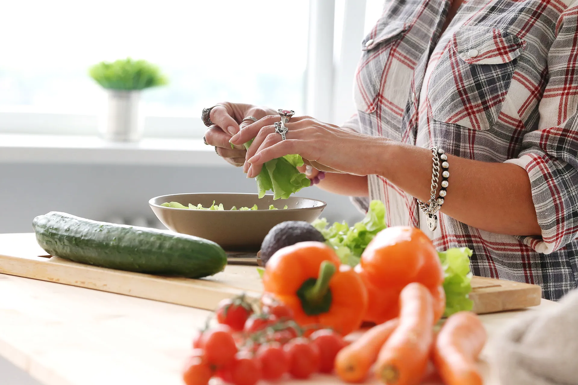 Frau bereitet in heller Küche einen frischen Salat mit Gurke, Paprika, Tomaten und Karotten zu – darmgesunde Ernährung im Alltag