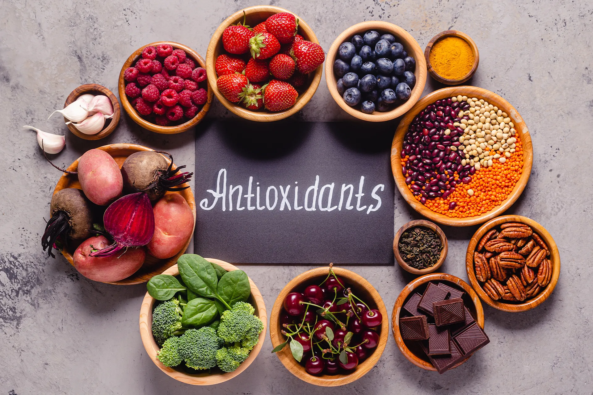 Antioxidantienreiche Lebensmittel mit Beeren, Brokkoli, Spinat, Roter Bete, Hülsenfrüchten, Pekannüssen und dunkler Schokolade in Holzschalen