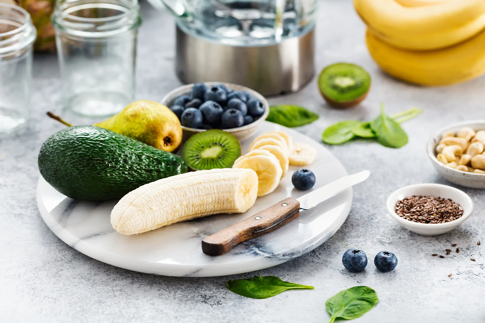 Mineralstoffreiche Lebensmittel mit Avocado, Banane, Kiwi, Birne, Blaubeeren, Spinat, Cashewkernen und Leinsamen auf einer Marmorplatte