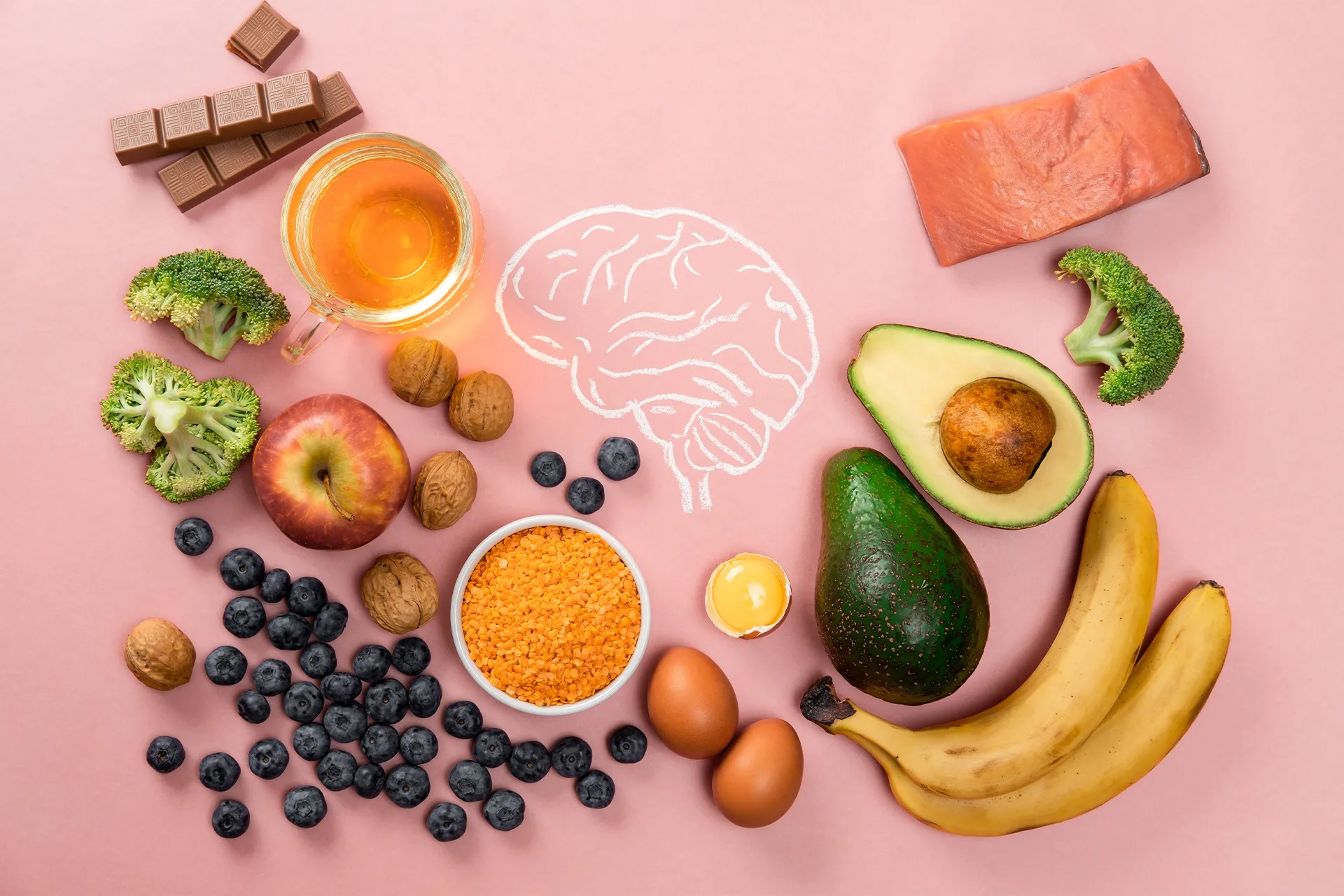 Nährstoffreiche Lebensmittel wie Lachs, Avocado, Walnüsse, Heidelbeeren, Eier, Brokkoli und Linsen rund um eine gezeichnete Gehirnskizze