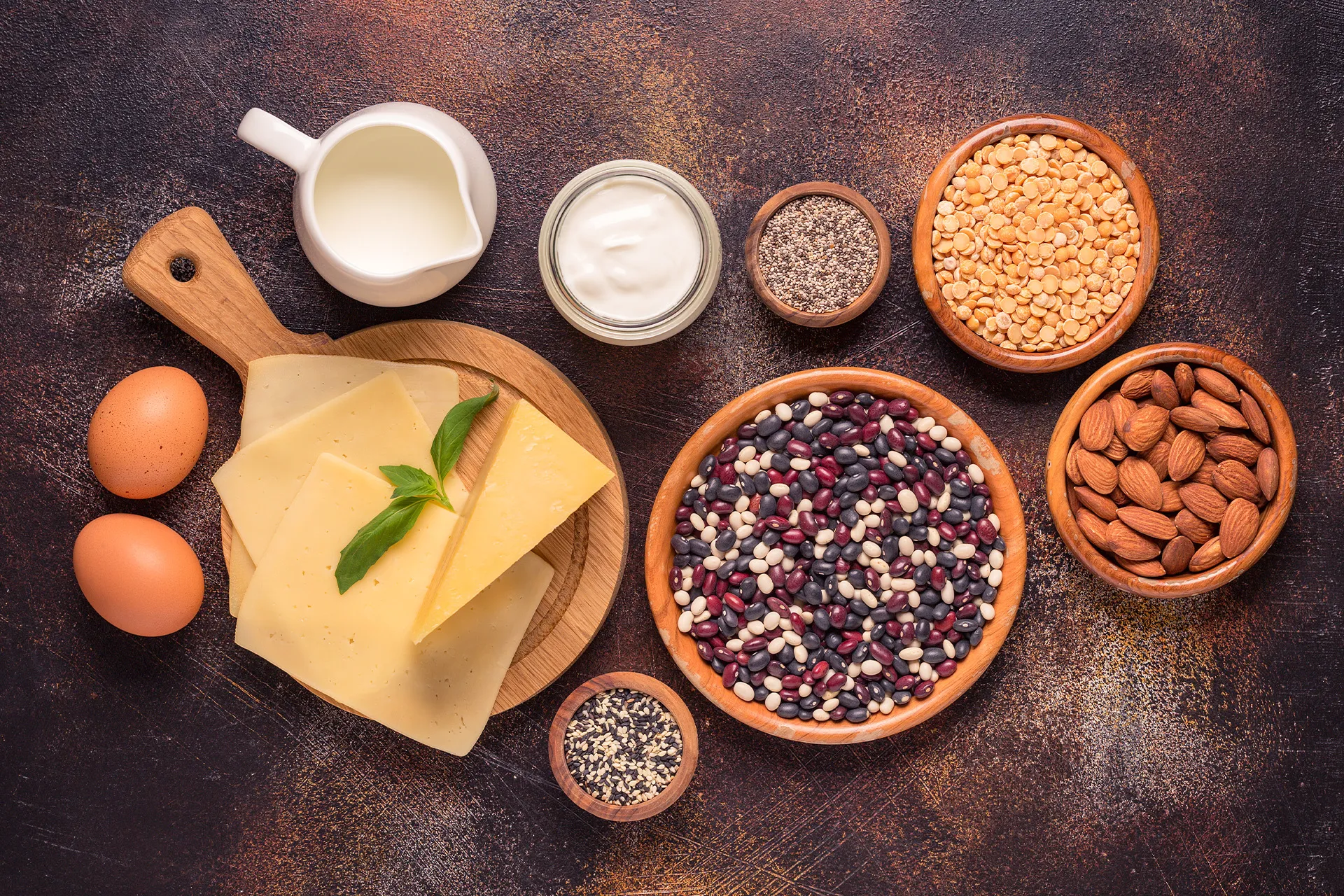 Eiweißreiche Lebensmittel wie Eier, Käse, Milch, Joghurt, Bohnen, Linsen, Mandeln und Samen in Schalen von oben fotografiert