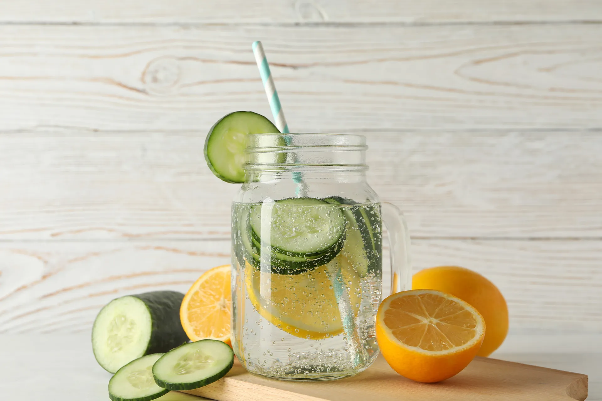 Glas mit frischem Wasser, Gurkenscheiben und Zitrone auf einem Holzbrett vor hellem Hintergrund – Anregung für eine abwechslungsreiche Trinkroutine